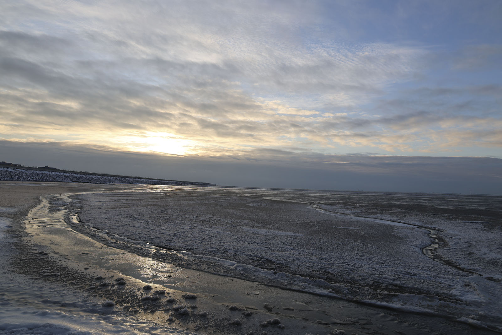 Winter tidal flats at low tide, ice on the sand, sun low on the horizon
